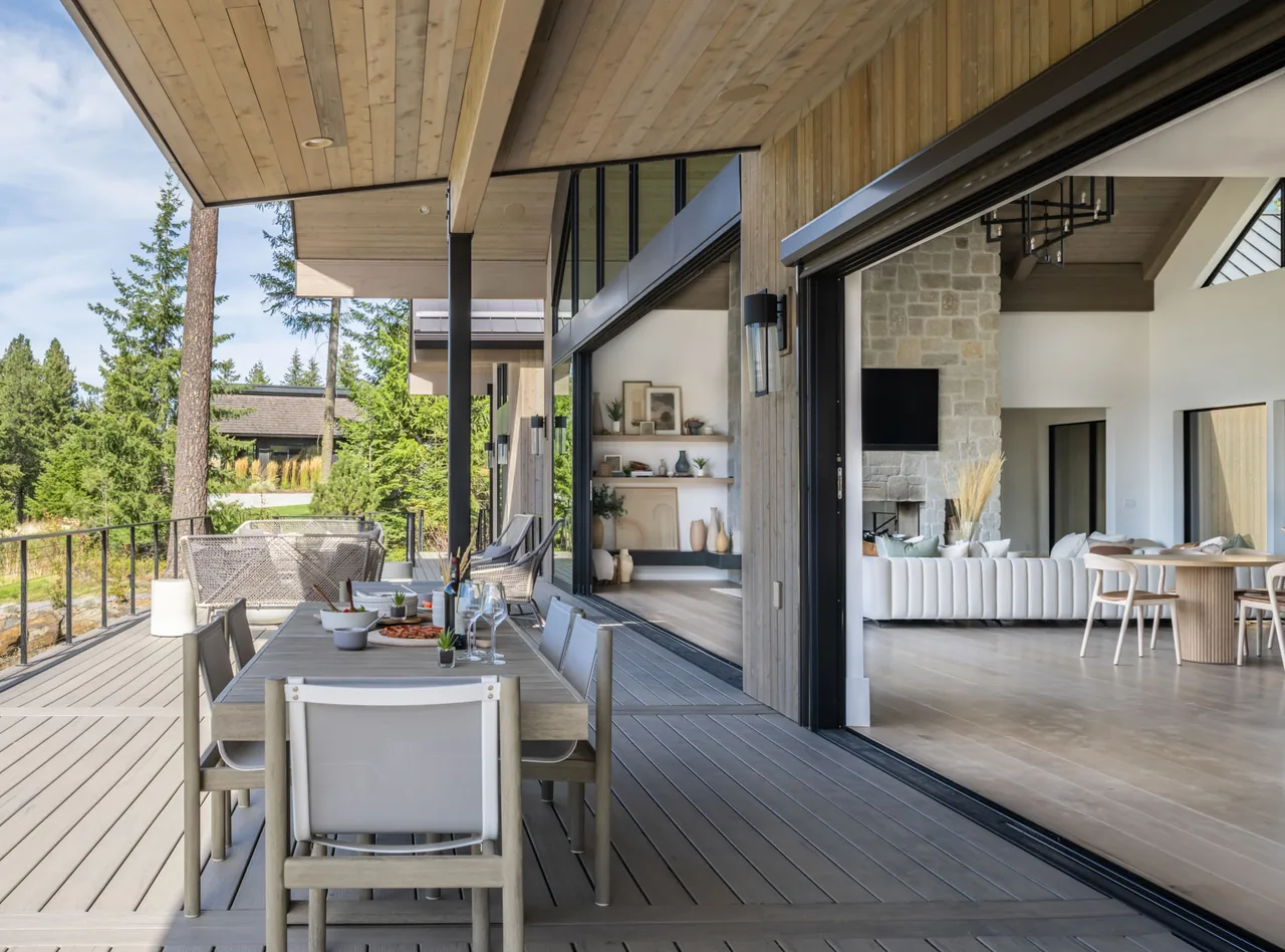View from the outdoor dining deck into the living room with a stone fireplace and vaulted ceiling in the Lakeside View project.