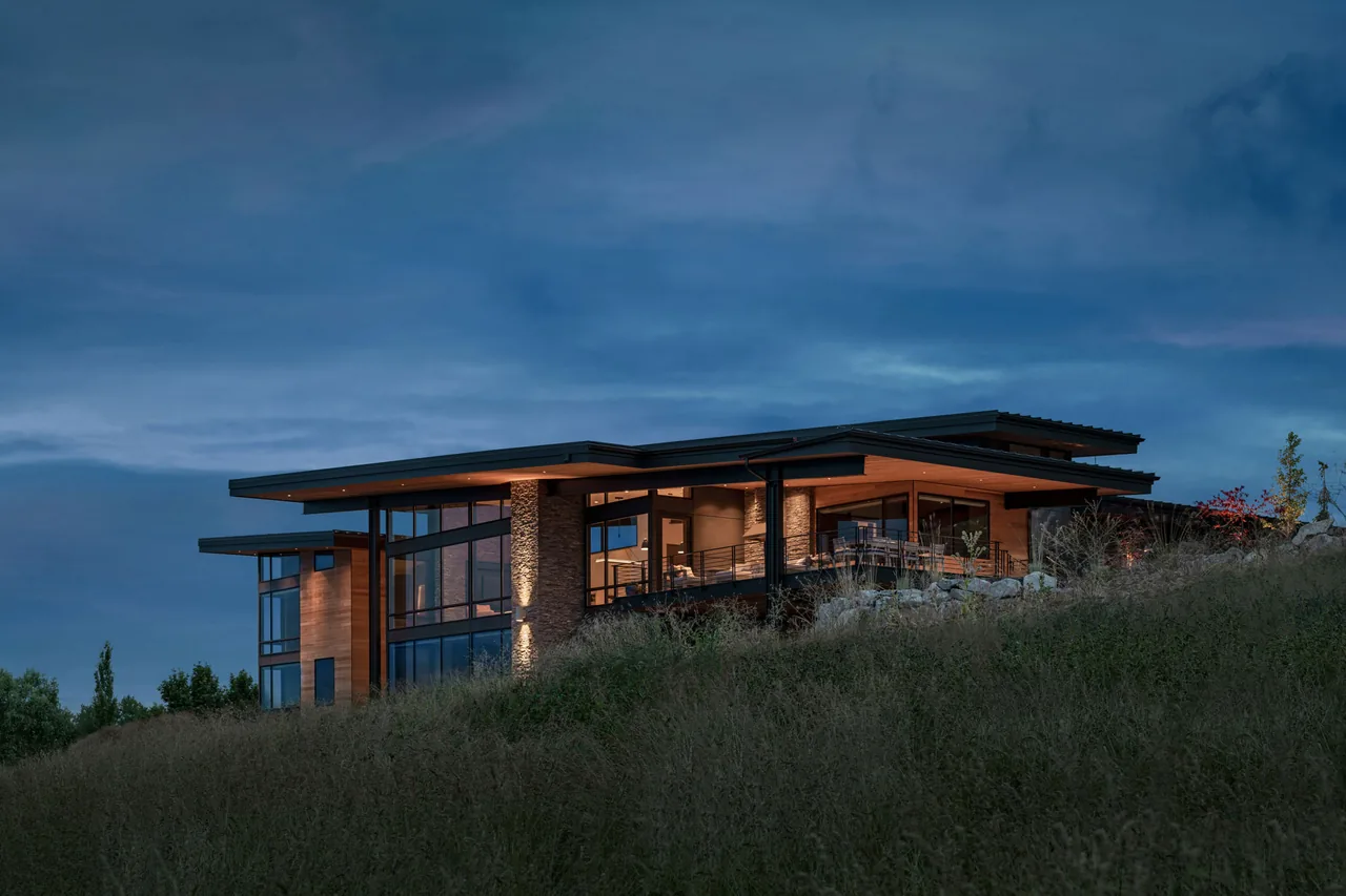 Saddle Mountain project by Uptic Studios features a modern hilltop home with flat roofs, stone walls, and expansive glazing at twilight.