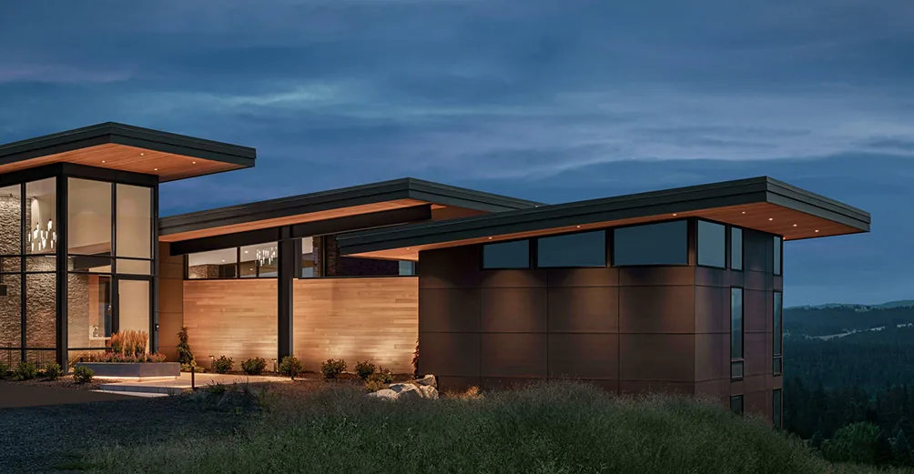 Saddle Mountain house exterior shows wood accent walls, black metal framing, and flat roofs with metal edges at twilight.