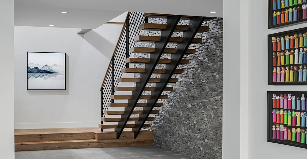 Modern floating stairs with wood treads and metal framework beside a textured stone wall at Saddle Mountain project.