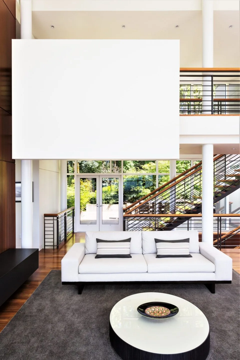 Living room with large windows, white sofa, and metal staircase in Hewett Street Residence by TVA Architects INC.