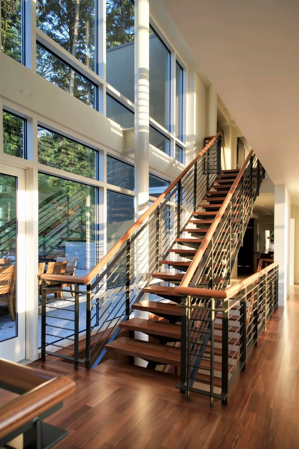 The Hewett Street Residence features a floating staircase with metal railings beside double-height windows.