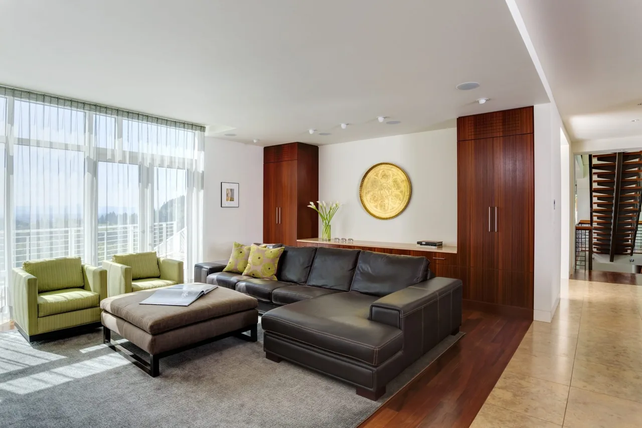 Living room featuring black leather sectional sofa, green armchairs, and floor-to-ceiling windows with sheer curtains.