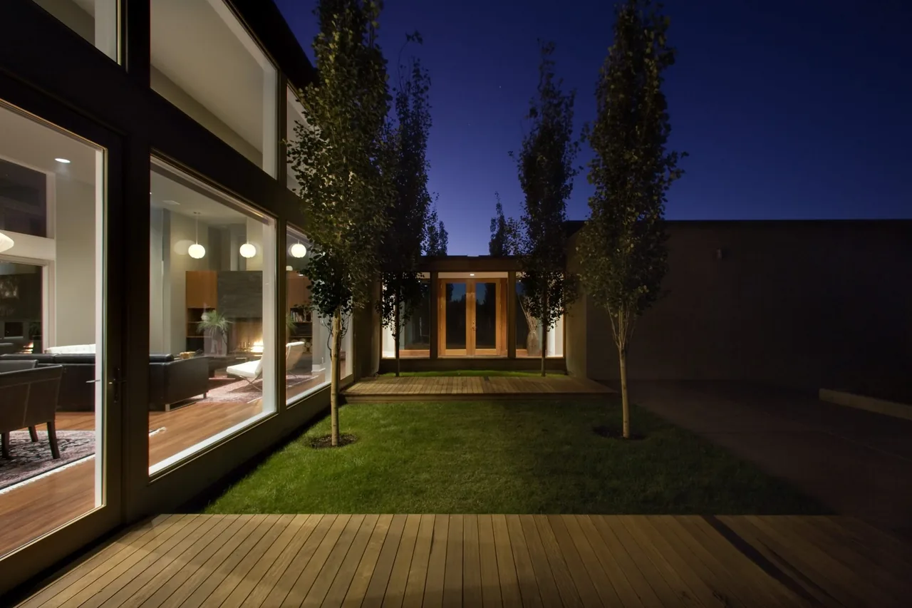 Fadjur Lane Residence features a modern courtyard with wood decking and large windows revealing interior living spaces.
