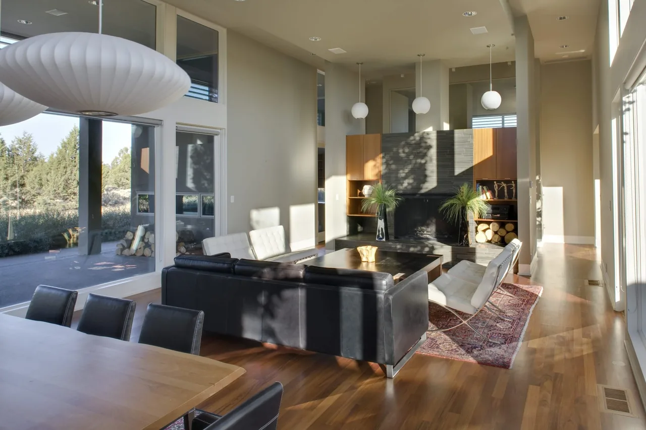 The Fadjur Lane Residence living area features high ceilings, a fireplace, and floor-to-ceiling windows with views of the outdoors.