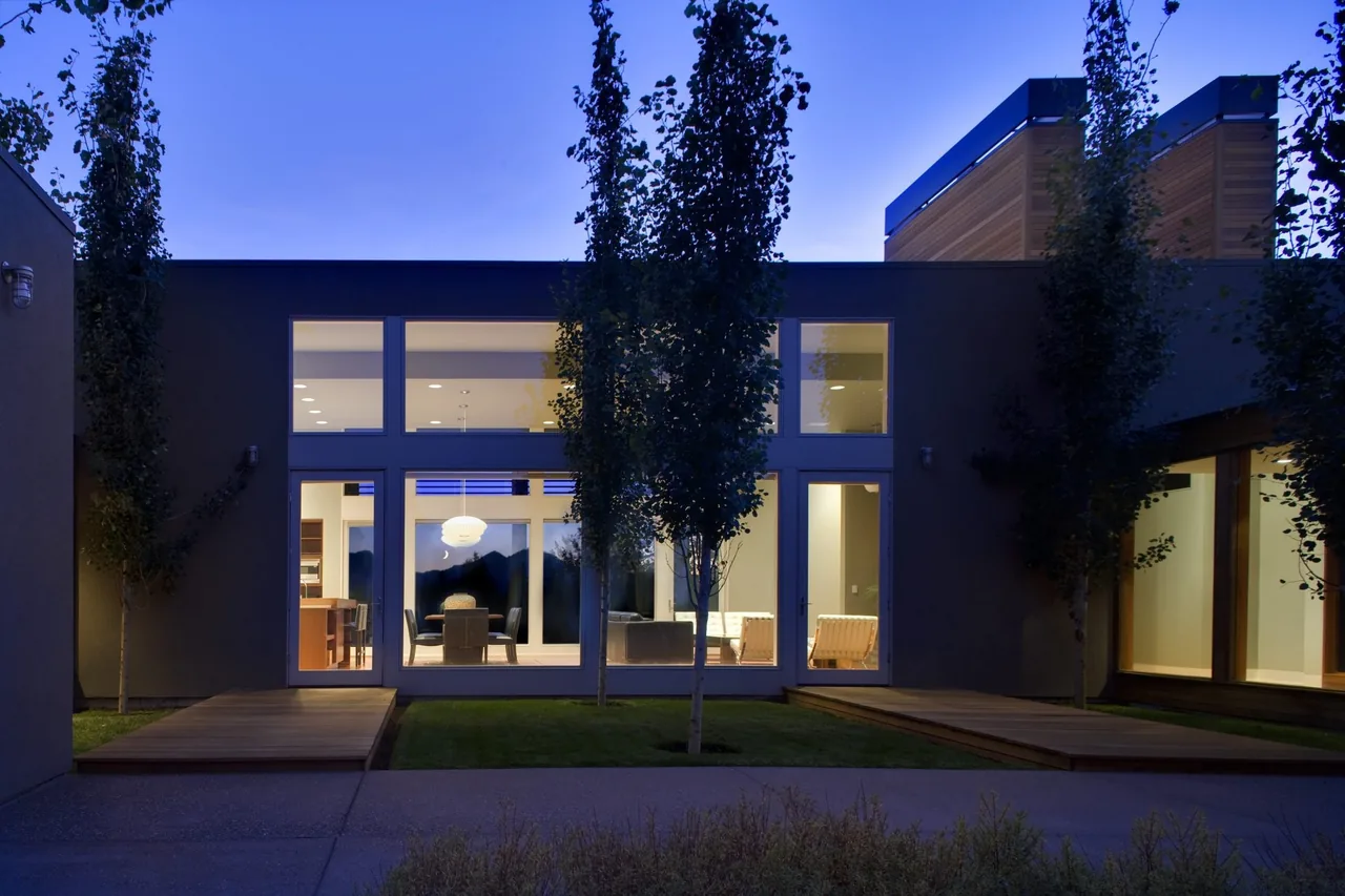 Exterior courtyard view of the Fadjur Lane Residence at dusk showing wood decks, glass windows, and slender trees.