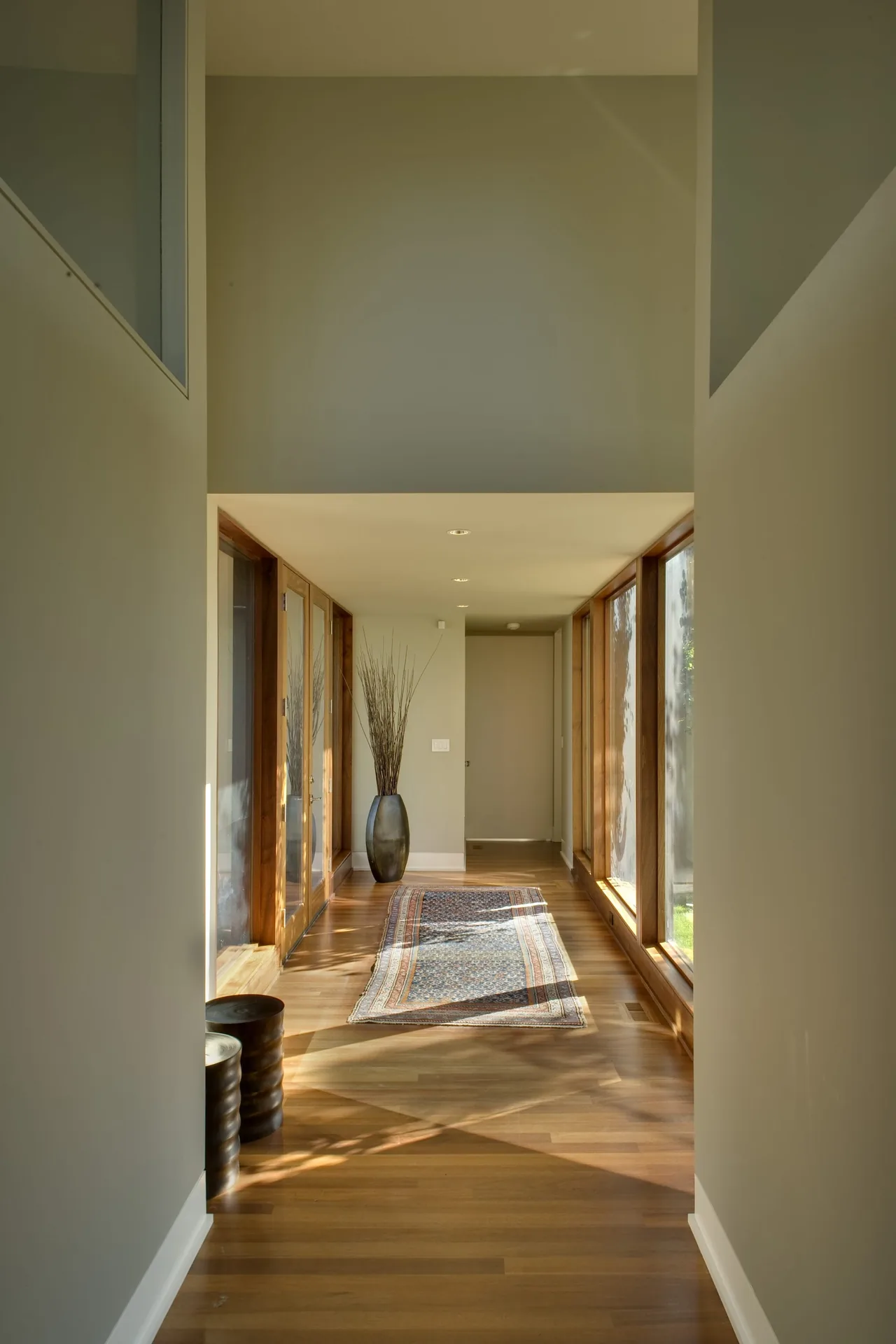 Hallway with wooden flooring, large windows, and a patterned runner rug in Fadjur Lane Residence by TVA Architects INC.