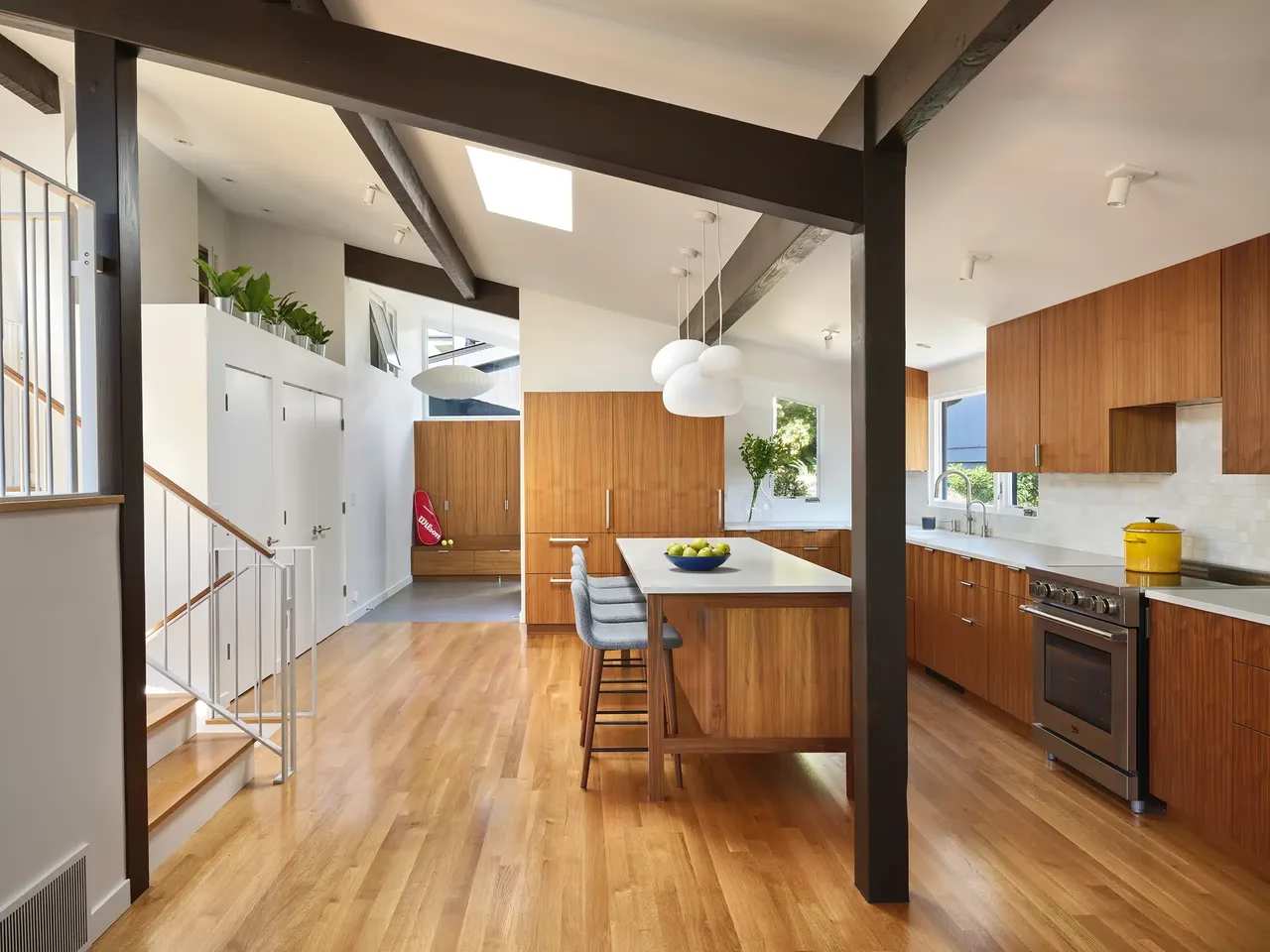 Mid-century modern kitchen with walnut cabinets, white countertops, hardwood floors, and exposed dark ceiling beams at Magnolia Mid-Century Modern.