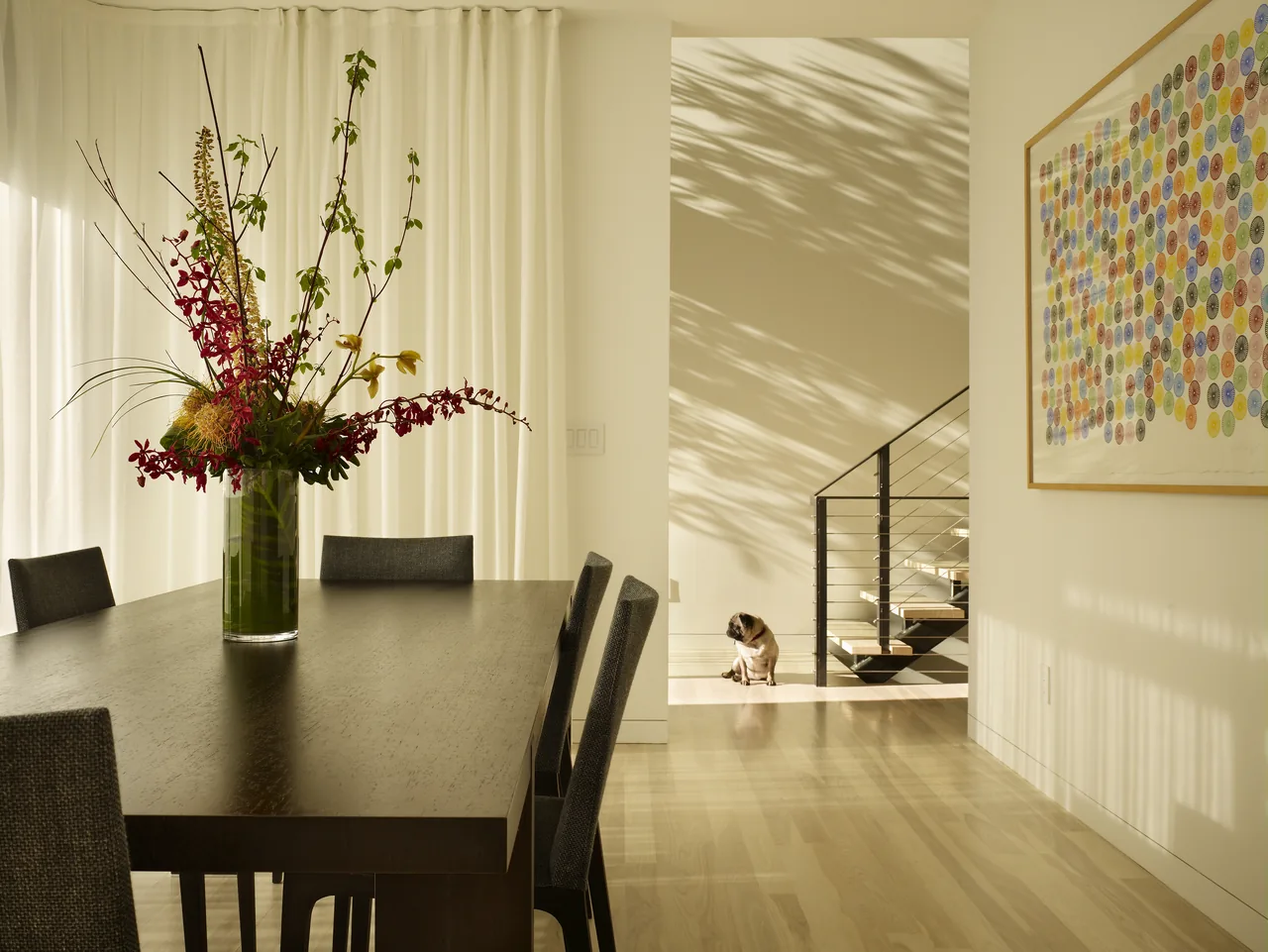 Dining room with dark wood table, floral centerpiece, and a modern open-riser stair with metal cable railing in the background.