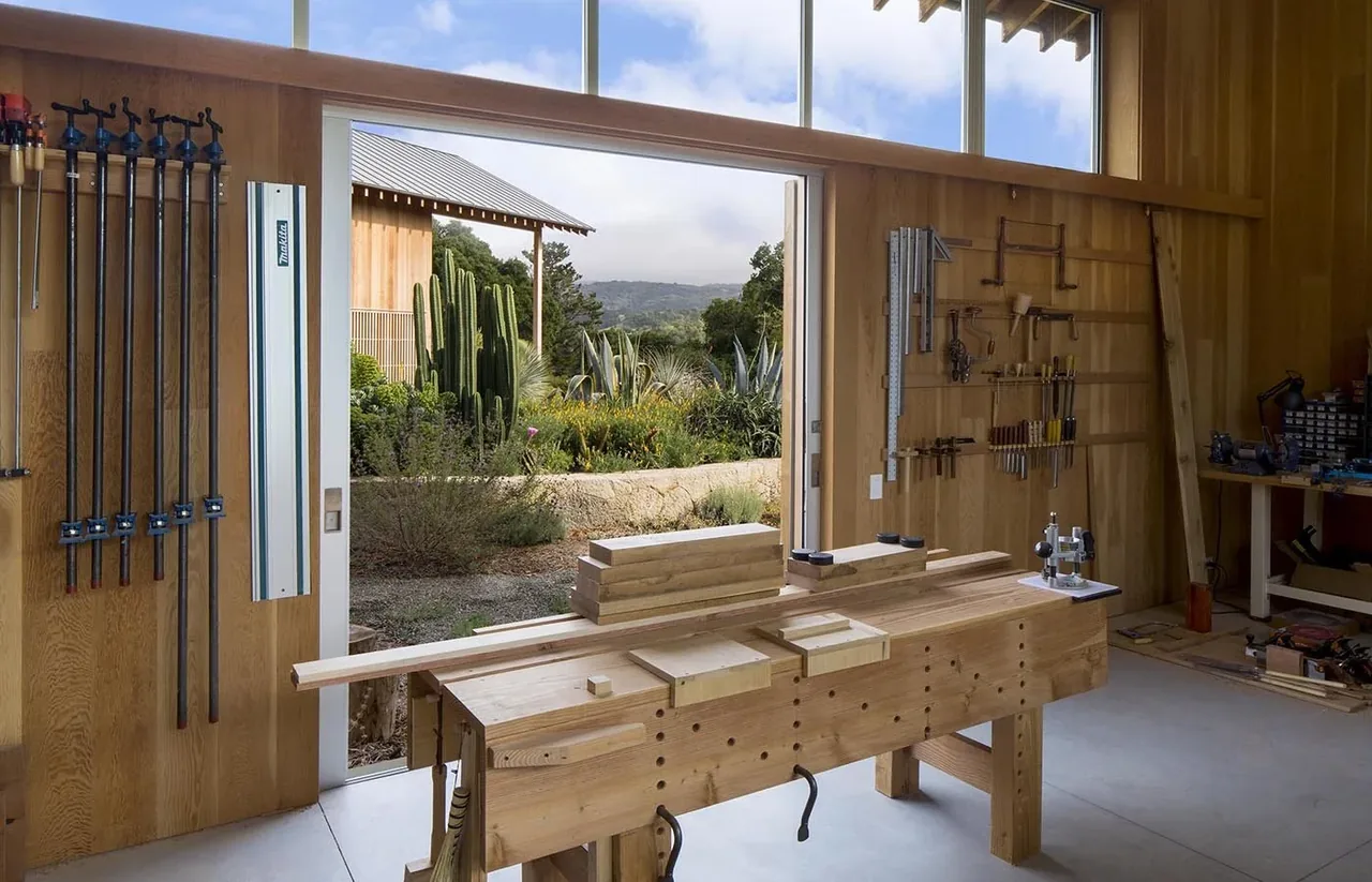 Woodworking space in South Bay Residence with an open sliding door revealing a xeriscape garden and raised stone planter outdoors.