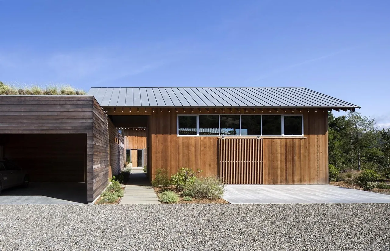 South Bay Residence features wood siding and a standing seam metal roof, with natural landscaping and large windows.