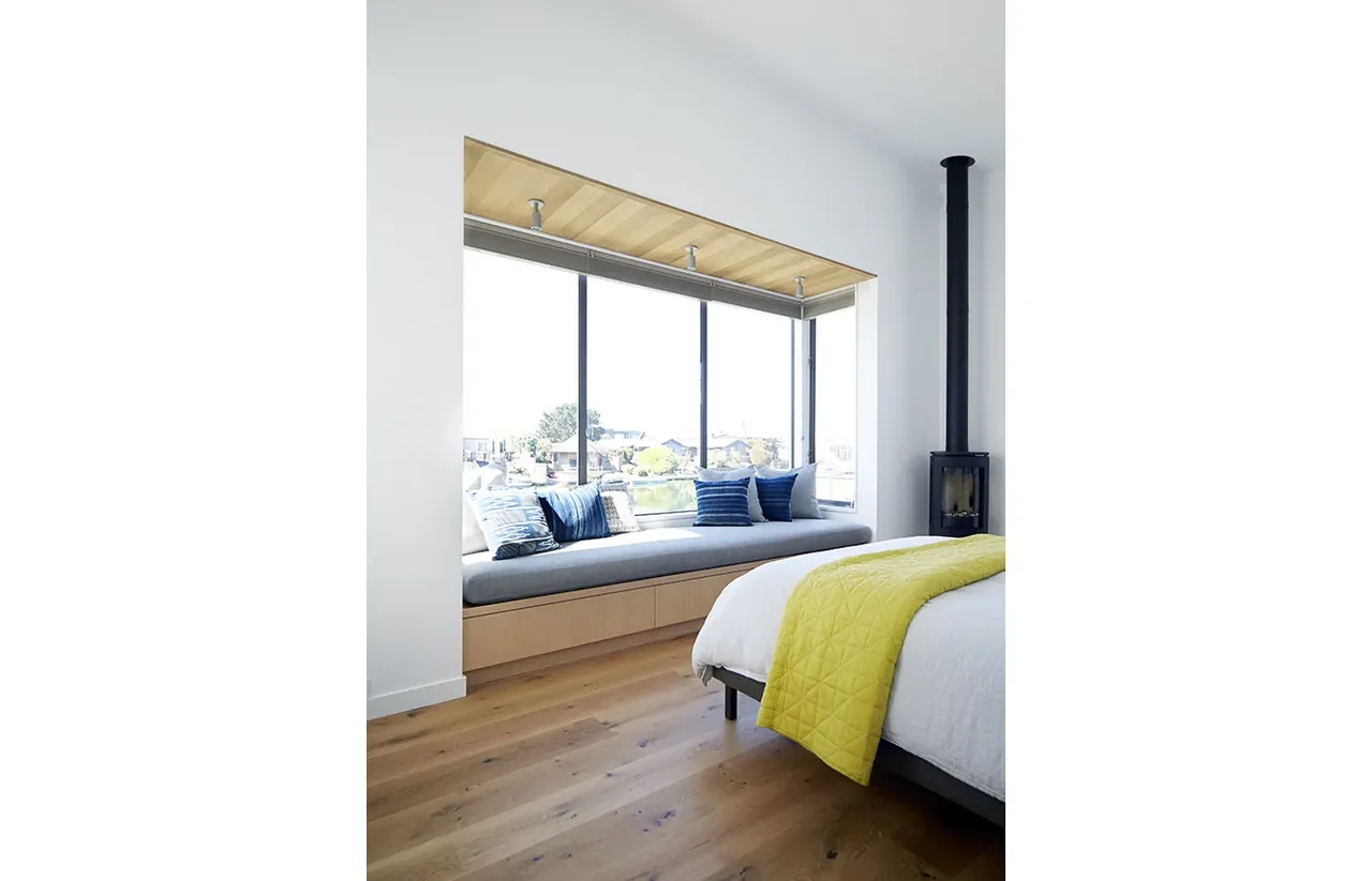 Bright bedroom with a built-in bench under floor-to-ceiling windows and a modern black fireplace.