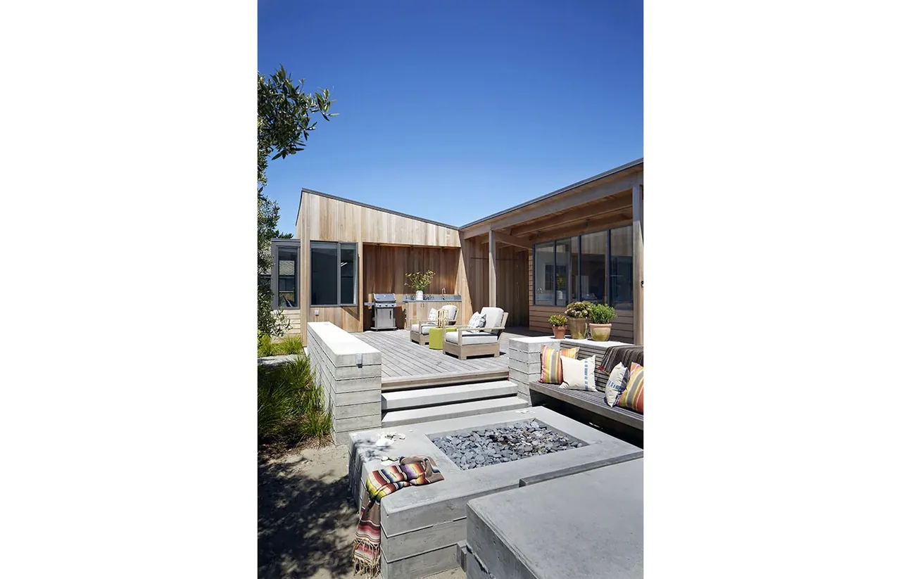 An outdoor living space featuring a sunken concrete fire pit surrounded by built-in seating and a wooden deck connected to the house.