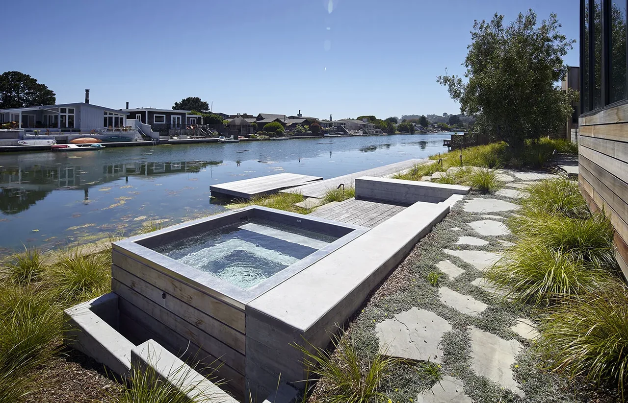 Waterfront outdoor living area featuring a built-in concrete bench and hot tub overlooking the lagoon at Stinson Beach Lagoon.