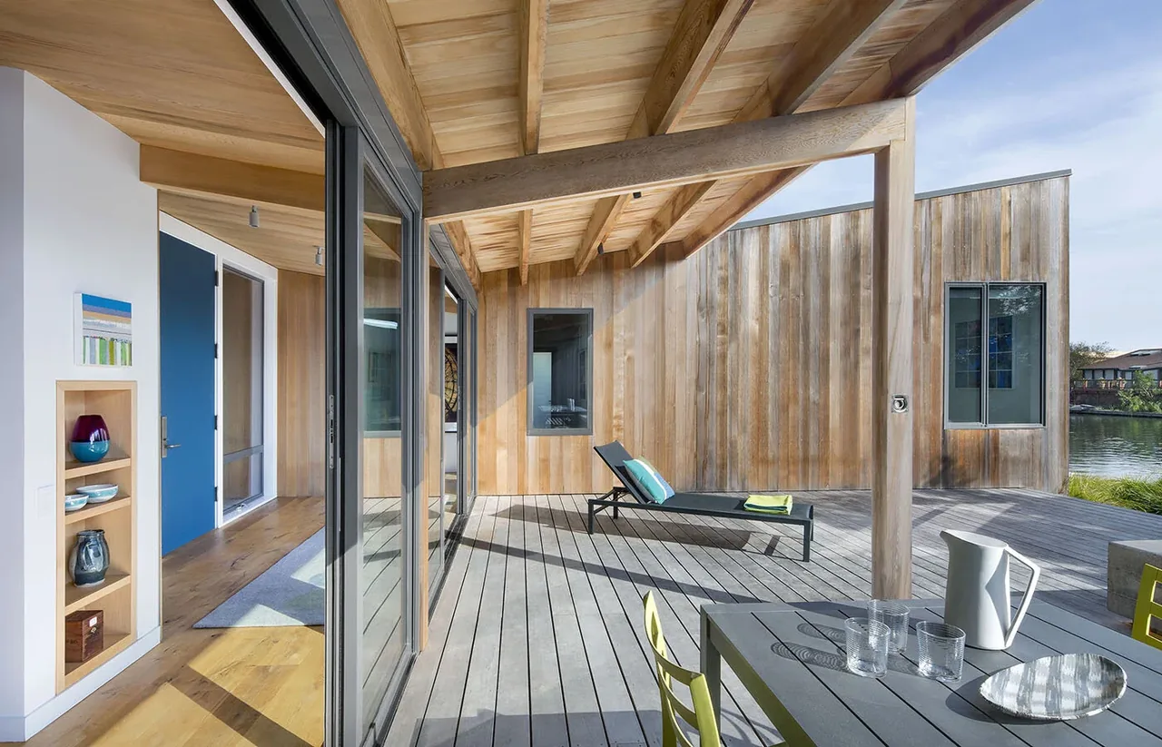 Outdoor living space with a wooden deck, lounge chair, and dining table by a waterfront.