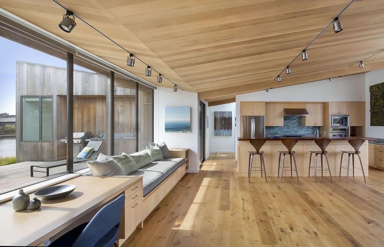 Stinson Beach Lagoon interior features an angled wood ceiling, built-in bench seating, and large sliding glass doors to a wooden deck waterfront view.