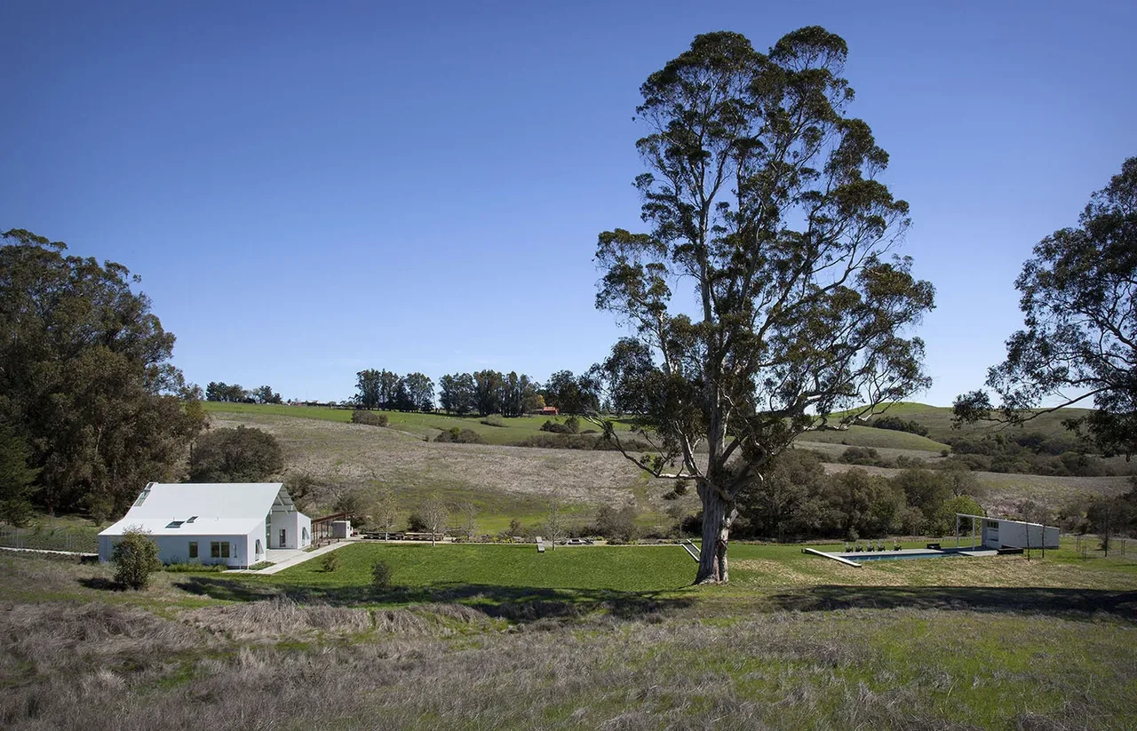 Hupomone Ranch features a white metal-roofed building set in a rural landscape with rolling hills and mature trees.