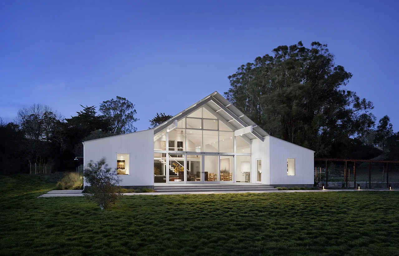 Hupomone Ranch by Turnbull Griffin Haesloop features a white exterior and large floor-to-ceiling glazing under a gable roof at twilight in San Francisco.