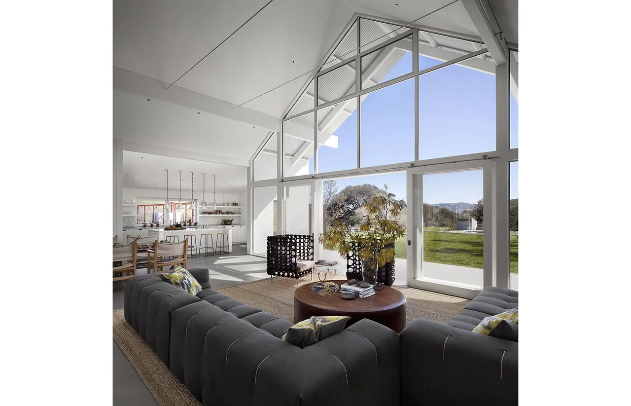 Living room with vaulted ceiling and large floor-to-ceiling windows looking out to a green landscape at Hupomone Ranch.