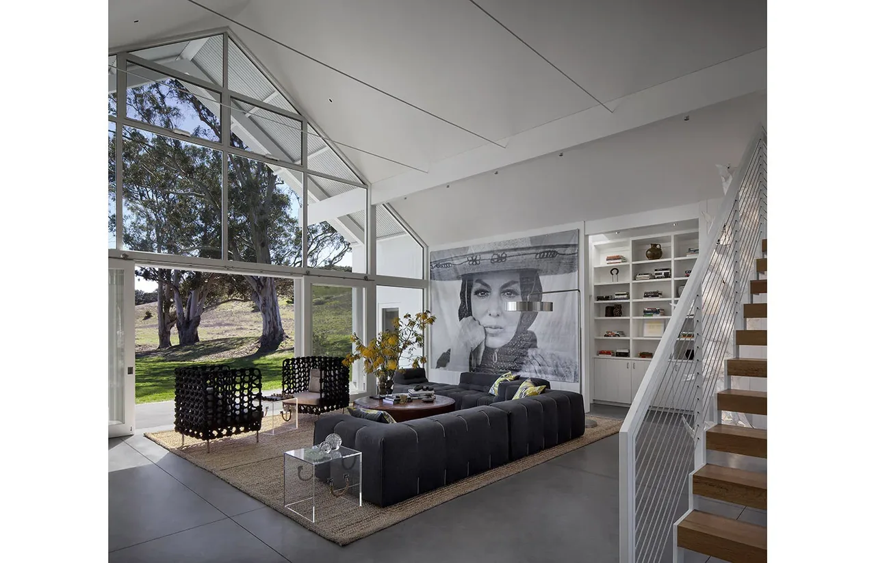 Interior living space of Hupomone Ranch features a large glass facade and exposed roof beams inside the vaulted ceiling.