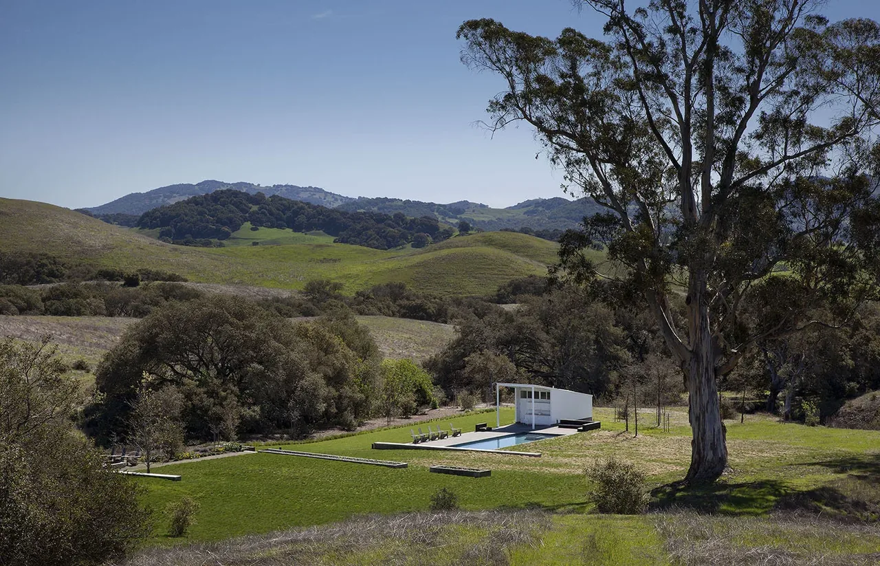 Modern pool house and swimming pool at Hupomone Ranch, set in open green hills with mature trees.