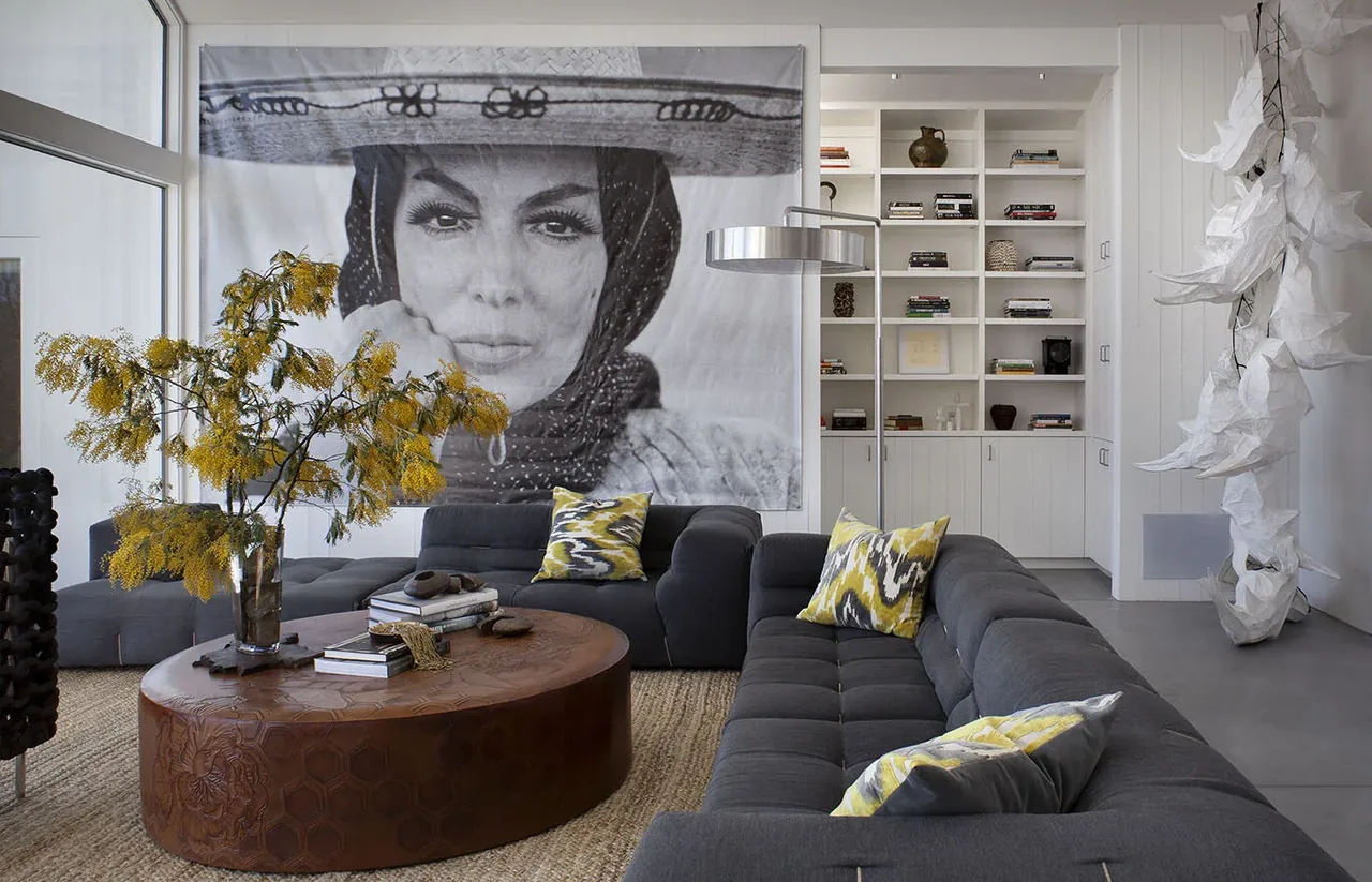 Living area with a large portrait, tufted dark sectional sofa, round patterned wood coffee table, and white built-in bookshelf cabinetry.