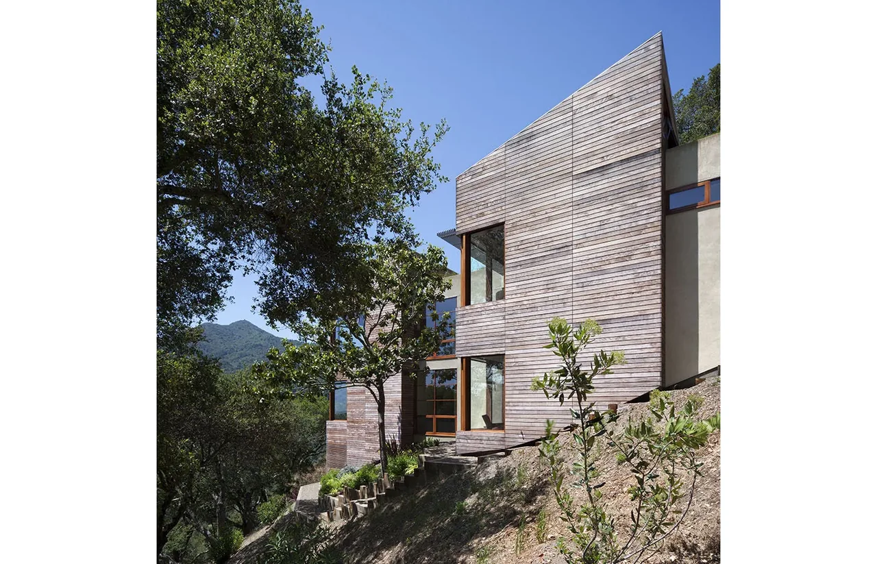 Kentfield Residence features wood siding and expansive glazing set into a hillside landscape with mountain views.
