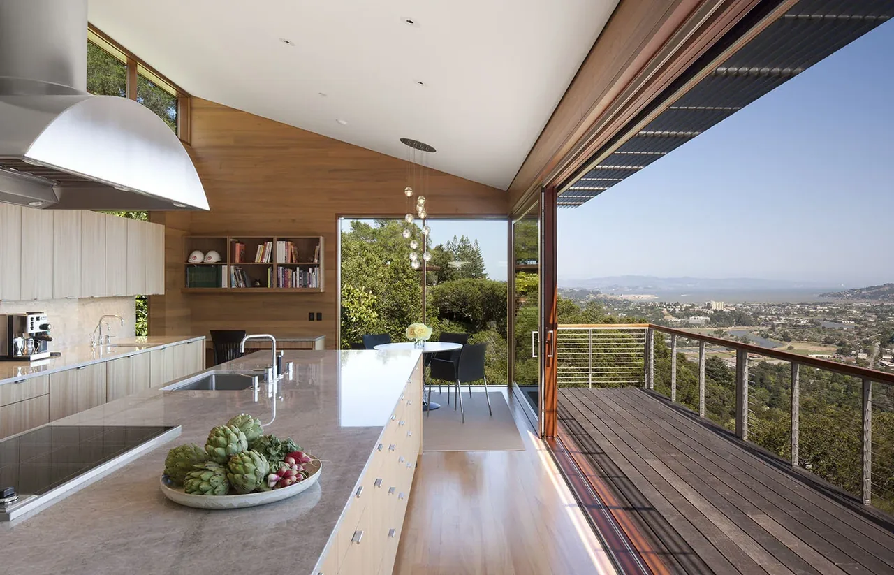 Kentfield Residence kitchen and dining space featuring large wood-framed sliding doors opening to a deck overlooking the valley and mountains.
