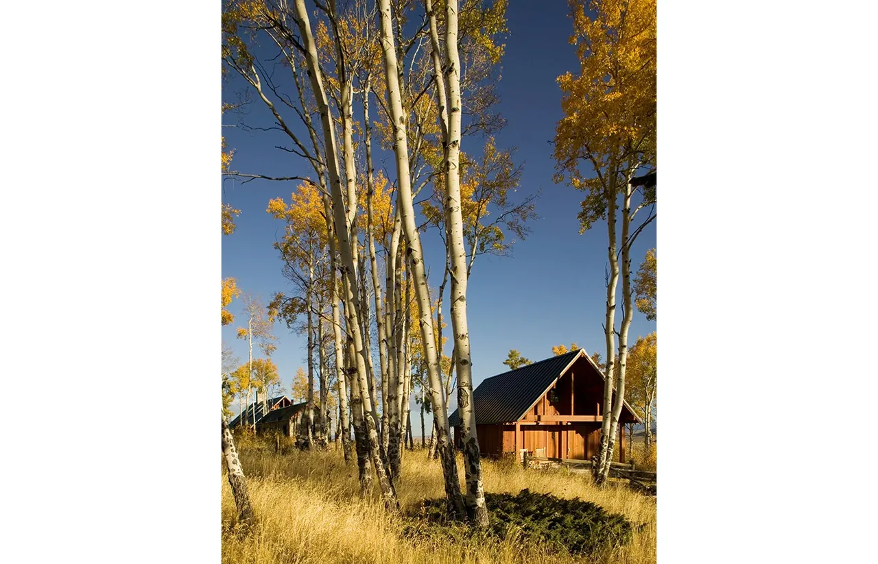 Colorado Ranch features wooden buildings with steep gable roofs amidst autumn foliage and open field.