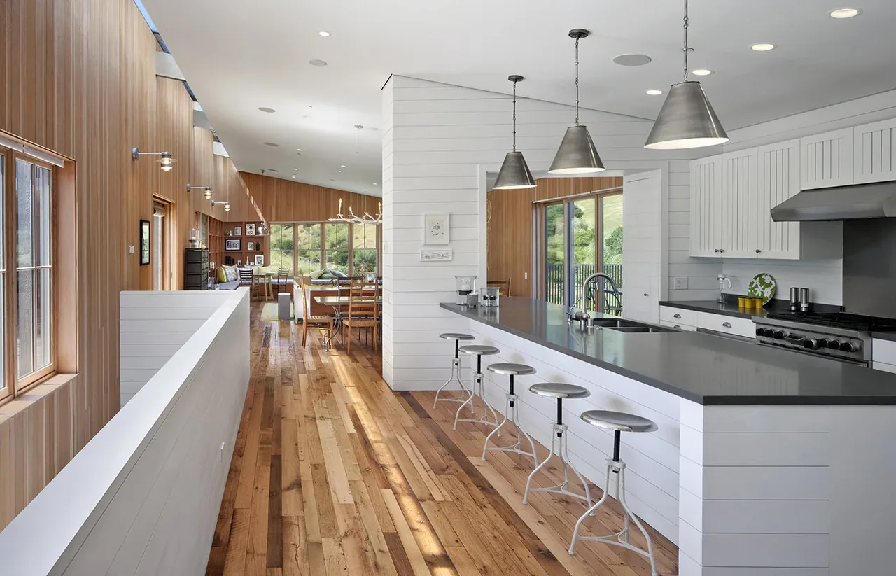 Open kitchen and dining space with wood paneling, hardwood floors, and pendant lighting in a ranch house design.