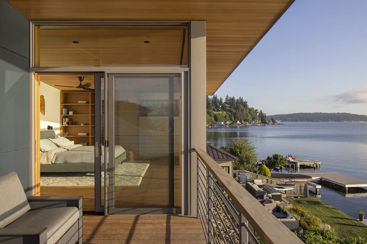 Outdoor balcony with metal railings and seating overlooks Lake Washington and docks, connected to a bedroom through sliding glass doors.