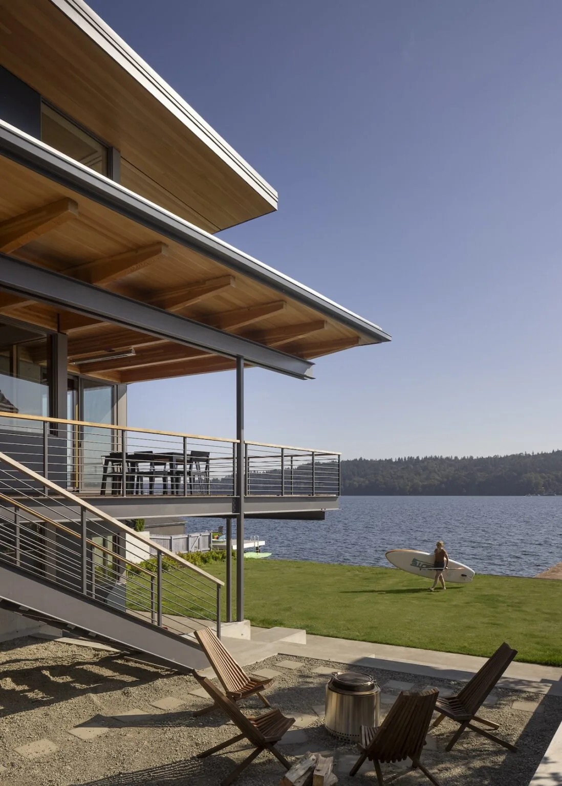 Exterior view of Lake Washington Residence showing the patio with wood chairs, metal railings, and water view.