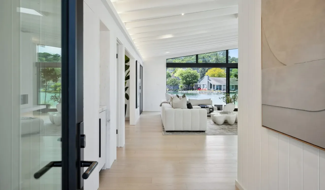 Living room with vaulted ceiling and floor-to-ceiling glazing features waterfront views through black-framed windows.