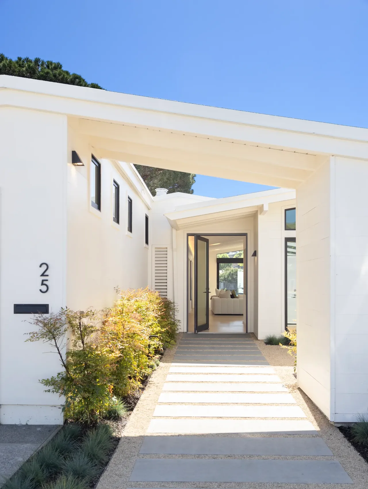 Modern white house entrance with black-framed windows and a pathway of concrete stepping stones in gravel.