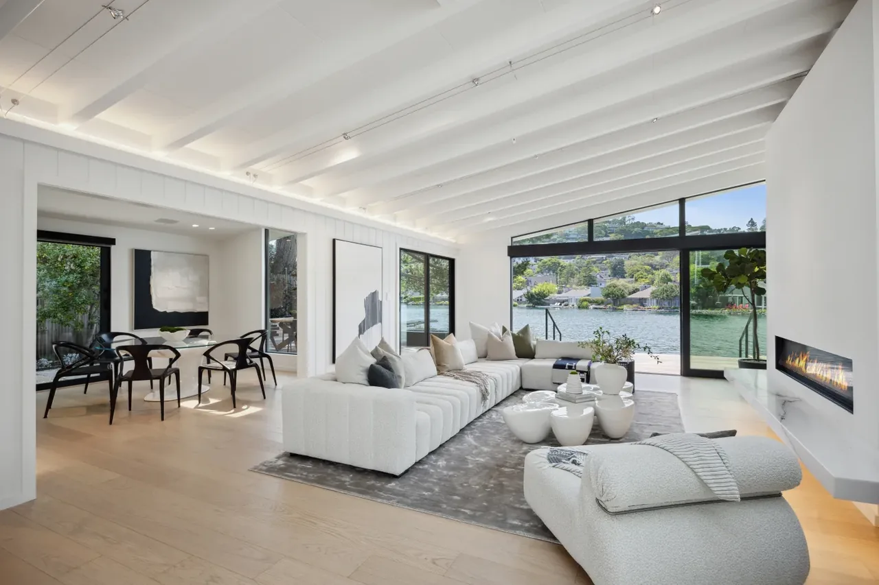 Living room featuring vaulted ceiling, floor-to-ceiling corner windows, and a linear fireplace with waterfront view.