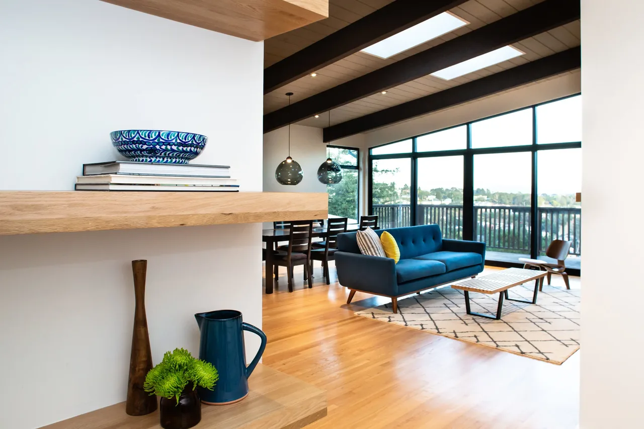 Living room features a blue sofa, geometric rug, and black window frames with a view to an outdoor balcony at Belmont Country Club.