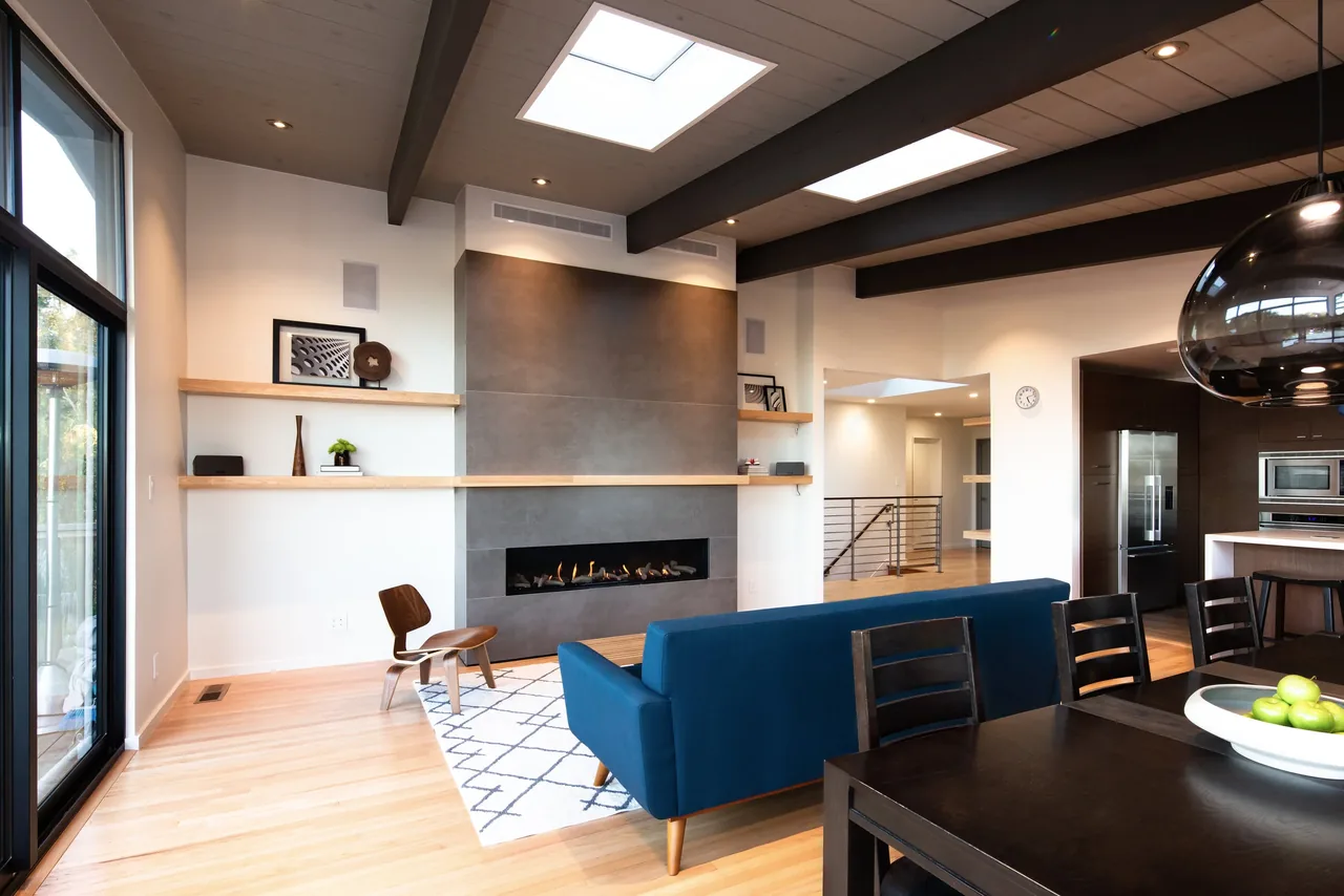 Open living area with a linear fireplace, wood shelving, skylights, and dark ceiling beams.