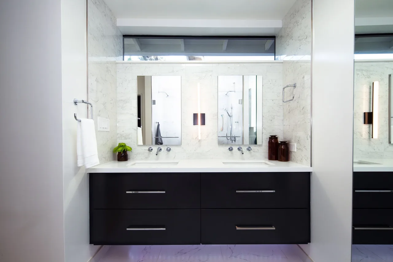 A bathroom featuring a floating double vanity with wall-mounted faucets and two rectangular mirrors, illuminated by a vertical light fixture.