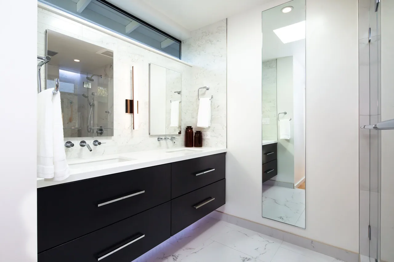 Bathroom featuring a double vanity with dark wood drawers and a full-length mirror near the entrance.