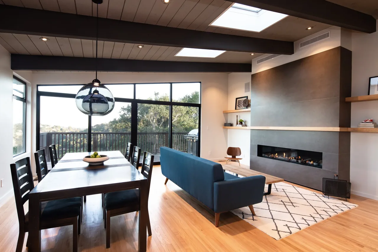 Modern living and dining space featuring a linear fireplace and floor-to-ceiling windows with a view of trees.