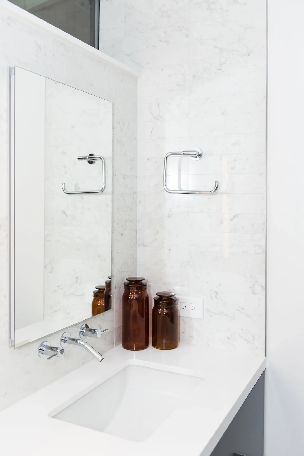 Bathroom sink area with white countertop, wall-mounted faucet, and two brown decorative jars on the corner.