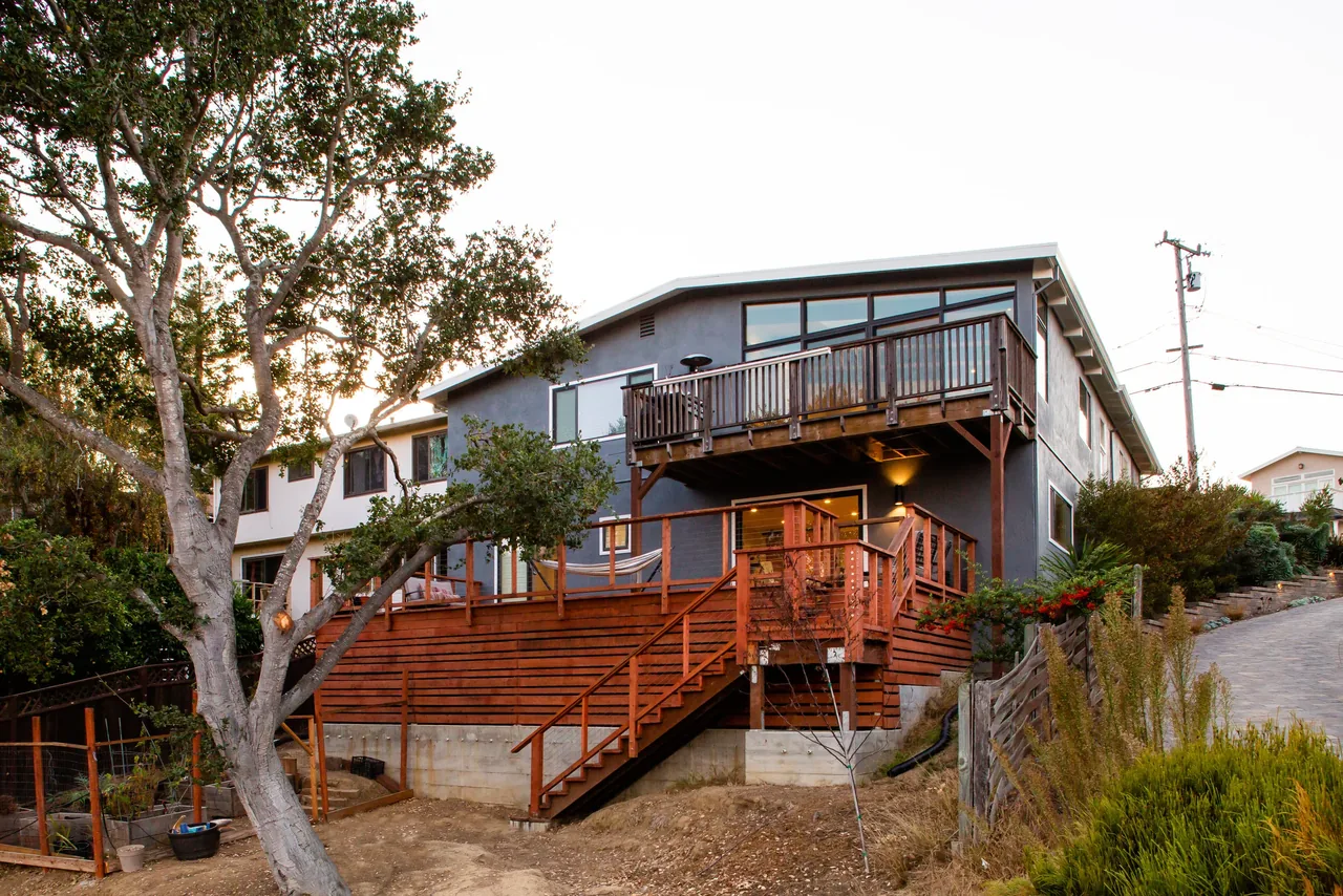 Rear exterior view of a two-story house showing wooden decks and stair with a concrete foundation base.
