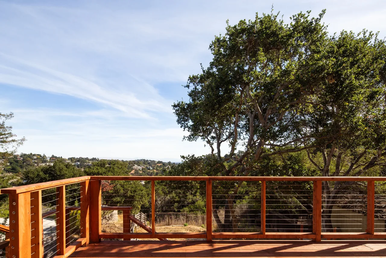 Wood deck railing with horizontal cables provides a clear view of the sloped yard and surrounding landscape.