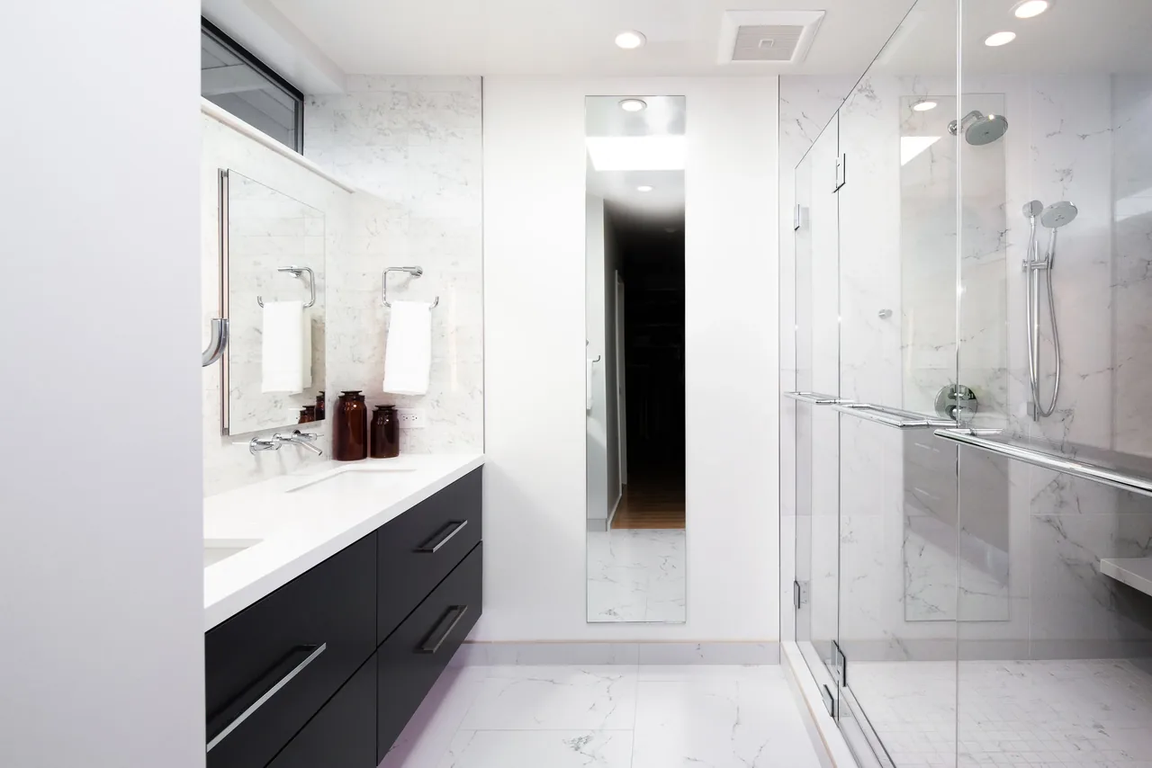 Bathroom featuring a floating double vanity with wall-mounted faucets and a glass shower with marble tile walls.