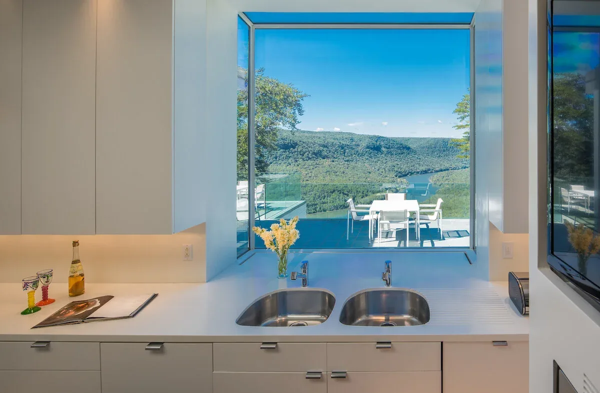 Kitchen sink area with large picture window framing river view and outdoor dining area on the deck.