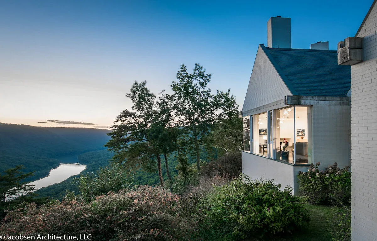 The Mills Residence features a white brick facade, glass bay window, and tall rectangular chimney with river views.