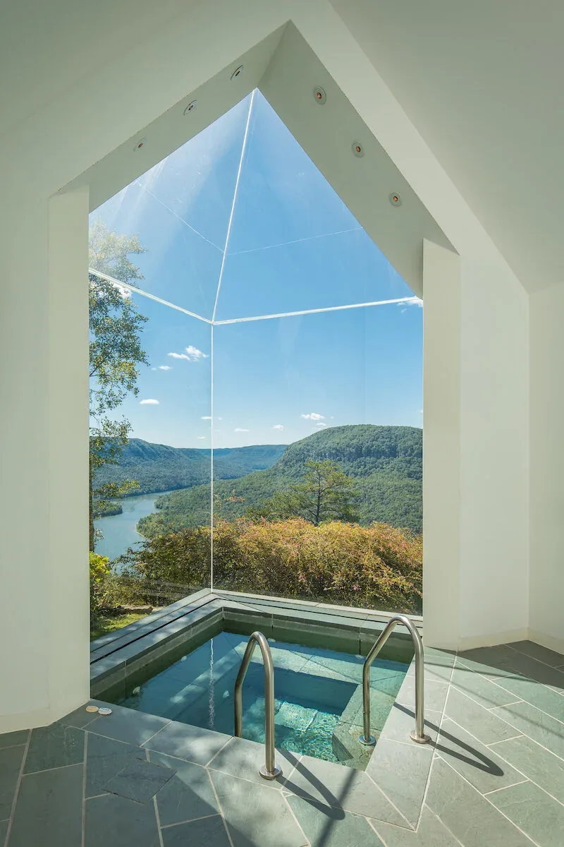 Indoor pool area framed by large floor-to-ceiling glazing with expansive views of a river and mountains.