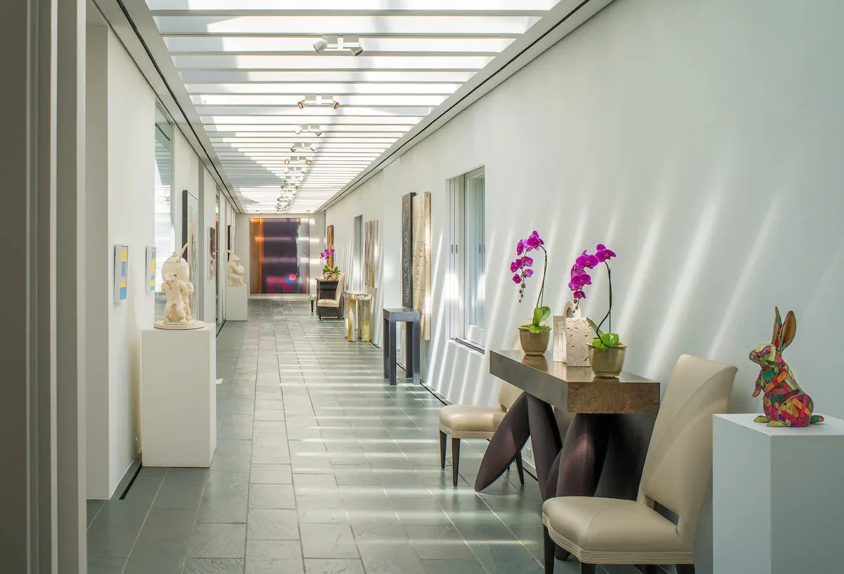 Symmetrical hallway featuring gray stone tile floor, skylight ceiling, and decorative furniture and art.