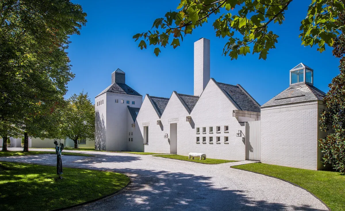 The Mills Residence features a symmetrical white brick facade with steep gable roofs and a tall chimney by Jacobsen Architecture, LLC.