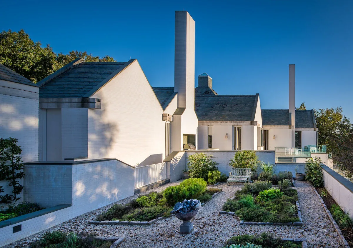 The Mills Residence features a white brick facade with tall rectangular chimneys and manicured garden beds.